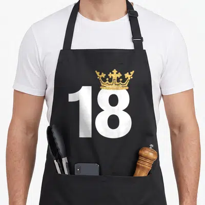 18th prince birthday apron - White number 18 with gold glittery crown centered on black fabric — shown on a black cotton canvas apron against a white background