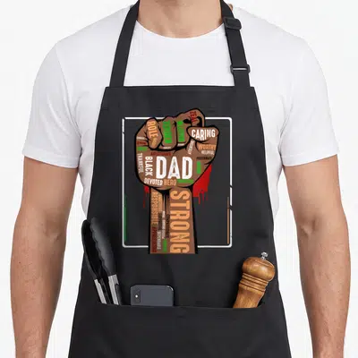 Melanin pride african american aprons - Brown fist with DAD STRONG text and red drips inside white border — shown on a black cotton canvas apron against a white background