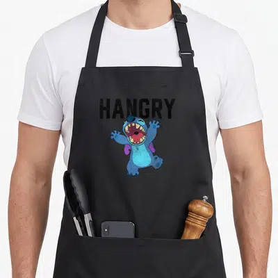 Hangry stitch apron - Blue cartoon character with open mouth under black HANGRY text on black apron — shown on a black cotton canvas apron against a white background