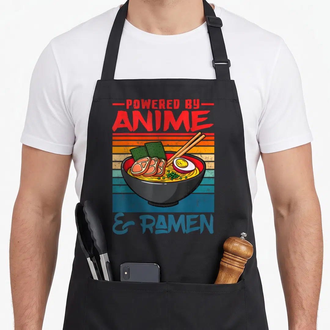 Powered ramen anime apron - Retro cartoon ramen bowl with chopsticks and striped background — shown on a black cotton canvas apron against a white background