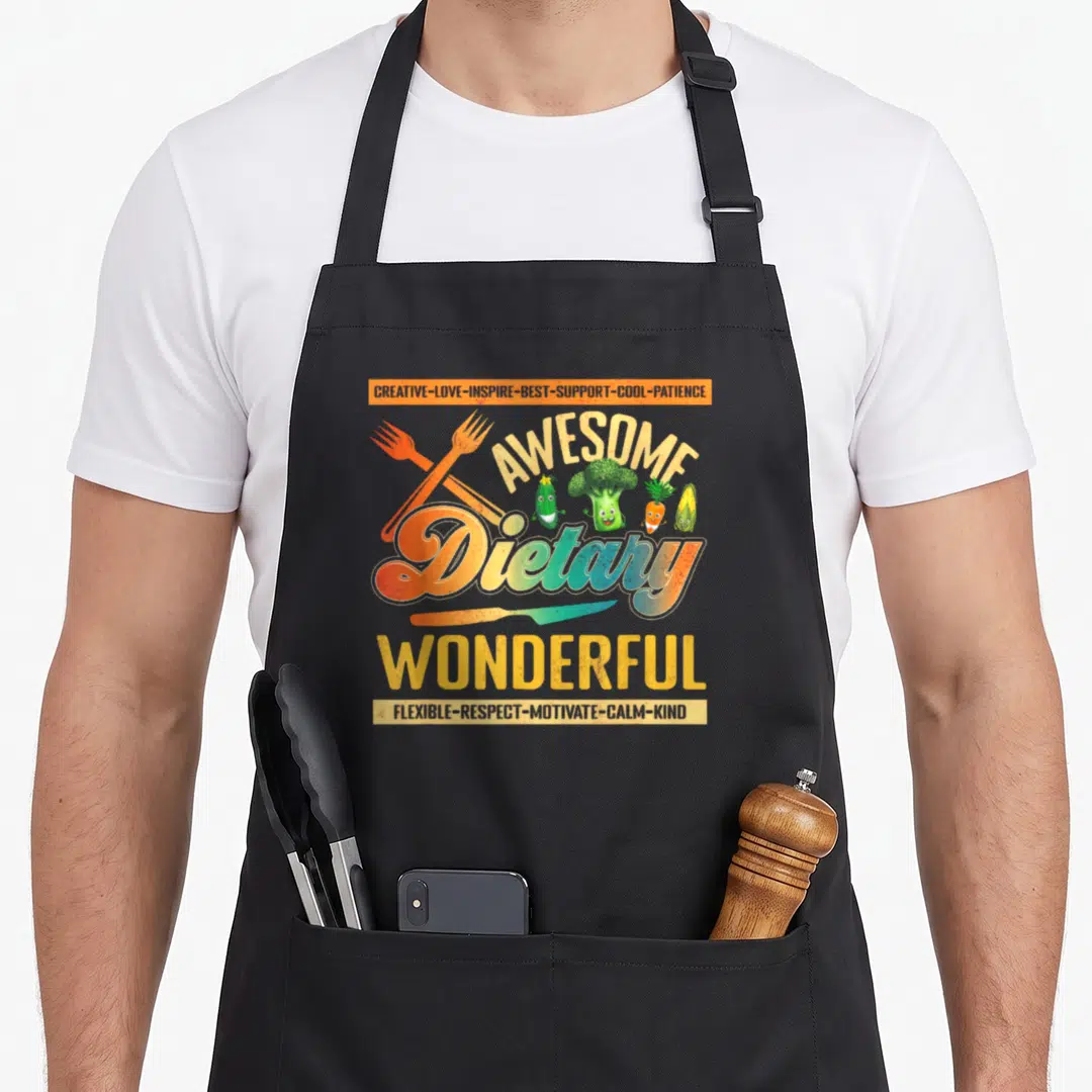 Week food service aprons - Awesome Dietary Wonderful text with cartoon vegetables, crossed forks, and knife in orange — shown on a black cotton canvas apron against a white background