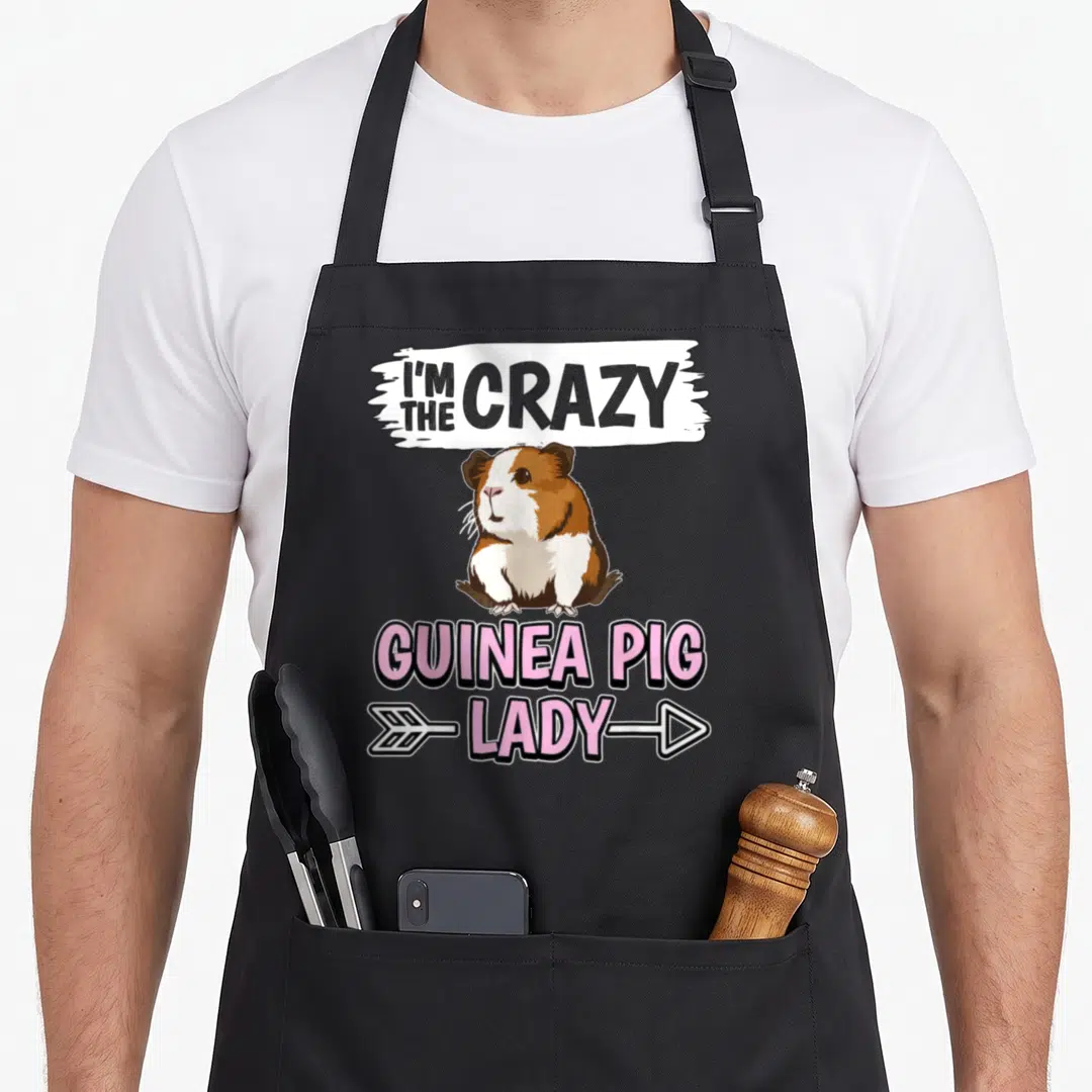 Cavy pig crazy guinea lady apron - Cartoon guinea pig in brown and white with pink and grey text reading I'm the crazy — shown on a black cotton canvas apron against a white background