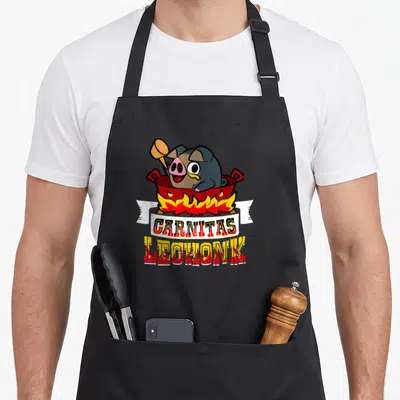 Fired animal apron - Cartoon pig in red pot with CARNITAS LECHONK text and flames — shown on a black cotton canvas apron against a white background