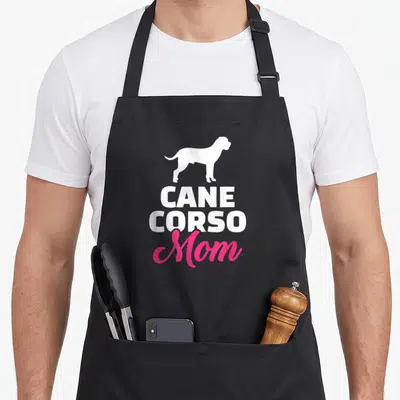 Vintage corso cane apron - White dog silhouette above stacked CANE CORSO Mom text in white and pink — shown on a black cotton canvas apron against a white background