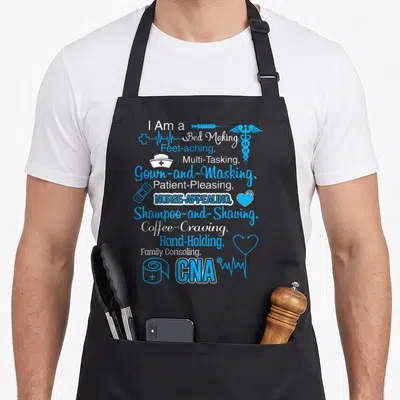 School nursing aprons - Stacked blue and white CNA job duties text with syringe, caduceus, bandage, toilet paper — shown on a black cotton canvas apron against a white background