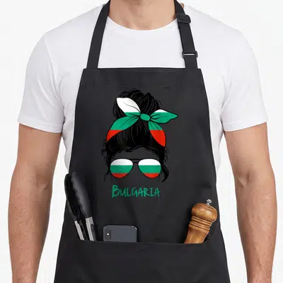 Bulgaria bulgarian apron - Cartoon woman with bun wearing sunglasses filled with Bulgarian flag colors above green — shown on a black cotton canvas apron against a white background