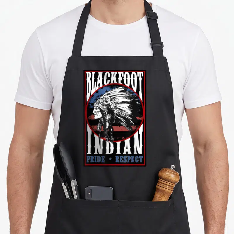 Blackfoot american flag apron - Distressed profile of man in headdress over circular flag with text Blackfoot Indian — shown on a black cotton canvas apron against a white background