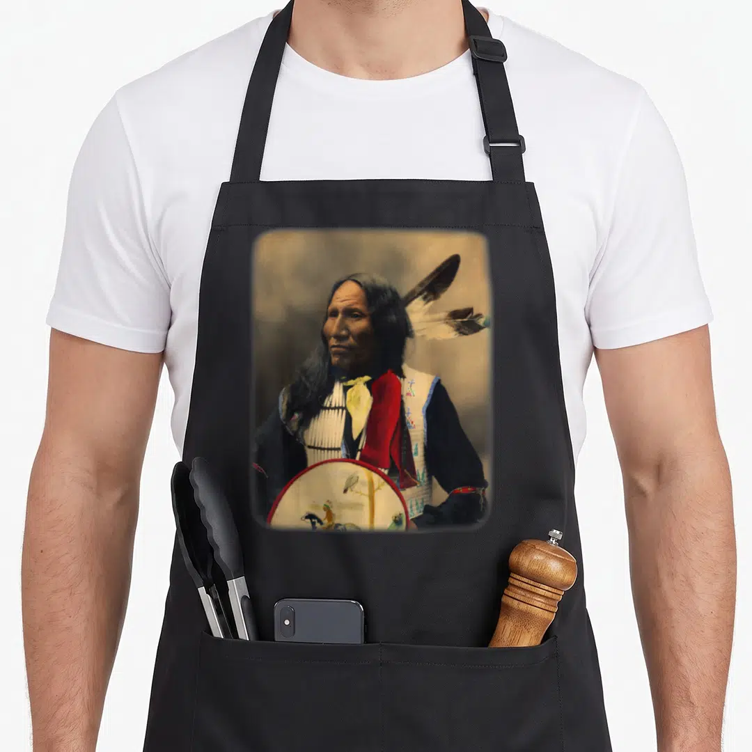 Oglala native american apron - Colorized portrait of a man holding a painted drum with red and yellow accents — shown on a black cotton canvas apron against a white background