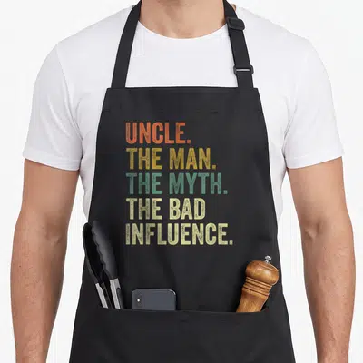 Myth cool uncle apron - Stacked colorful text UNCLE THE MAN THE MYTH THE BAD INFLUENCE on black background — shown on a black cotton canvas apron against a white background