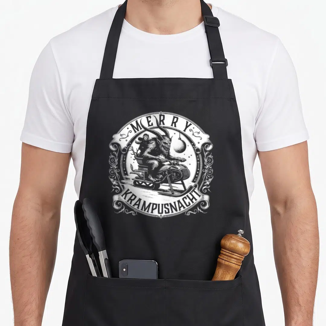 Krampusnacht snowmobile girl apron - White line art of Krampus on a sled with Merry Krampusnacht text in circular frame — shown on a black cotton canvas apron against a white background