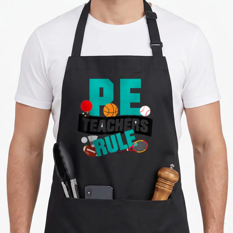 Rule teacher apron - PE TEACHERS RULE text with basketball, racket, football, and baseball in cartoon style — shown on a black cotton canvas apron against a white background