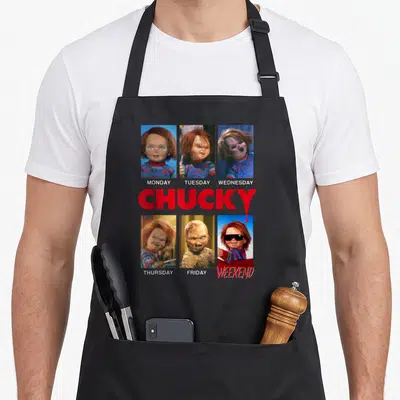 Mood week apron - Six Chucky photos in grid with red CHUCKY text and day labels — shown on a black cotton canvas apron against a white background