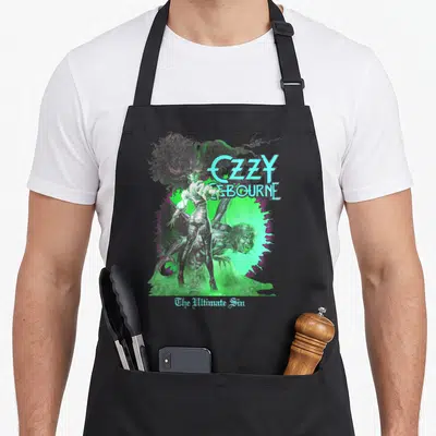 Sunburst ultimate apron - Ozzy Osbourne The Ultimate Sin cartoon art with green smoke and monster — shown on a black cotton canvas apron against a white background