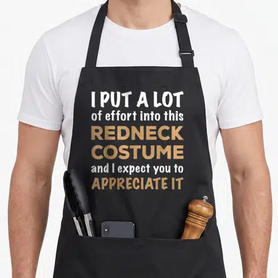 Halloween quick apron - White and tan stacked typography reading I put a lot of effort into this redneck costume and I — shown on a black cotton canvas apron against a white background