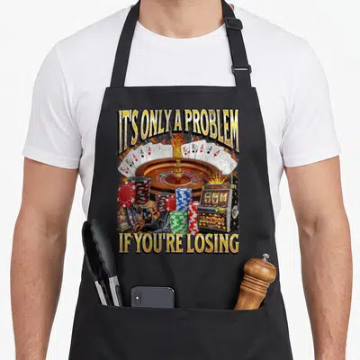 Losing problem funny apron - Man at roulette wheel with fire, cards, chips, and slot machine under sarcastic text — shown on a black cotton canvas apron against a white background