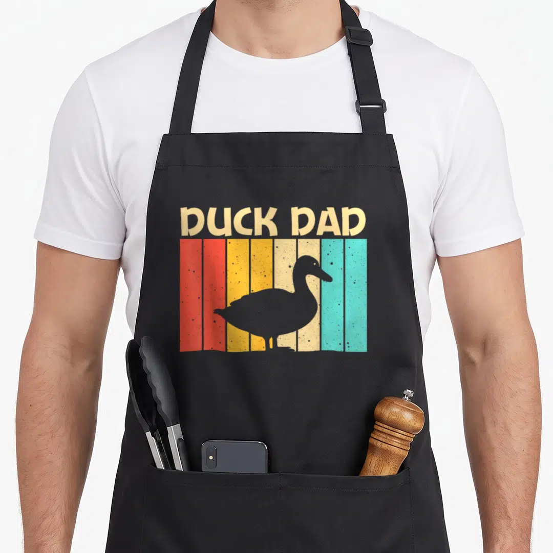 Farmer cotton duck apron - Retro DUCK DAD text over red orange yellow teal stripes with grey duck silhouette — shown on a black cotton canvas apron against a white background