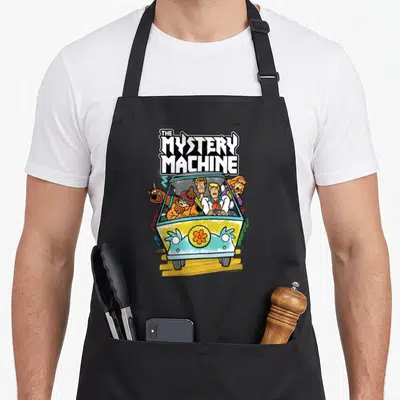 Vintage mystery machine apron - Cartoon van with stacked text, characters inside, and an orange flower on the front — shown on a black cotton canvas apron against a white background