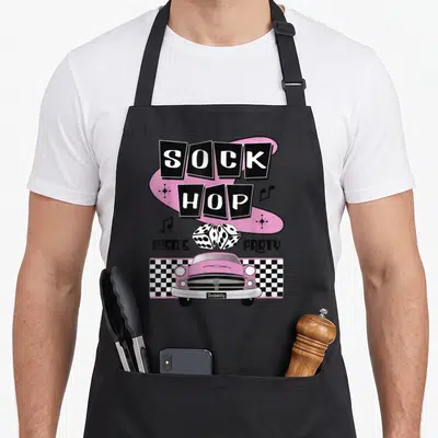Dance rockabilly apron - Sock Hop text, dice, pink car, and checkered pattern in pink and black — shown on a black cotton canvas apron against a white background