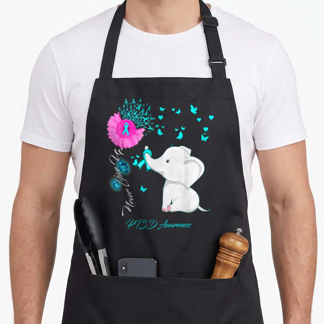 Elephant ribbon apron - White elephant holding cyan ribbon next to pink flower releasing hearts and butterflies — shown on a black cotton canvas apron against a white background