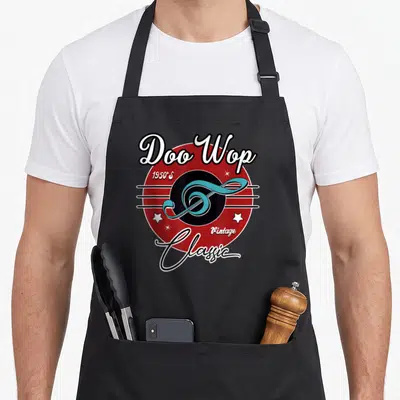 Doo wop rockabilly apron - Light blue treble clef over red circle with black center, white text Doo Wop 1950S Vintage — shown on a black cotton canvas apron against a white background