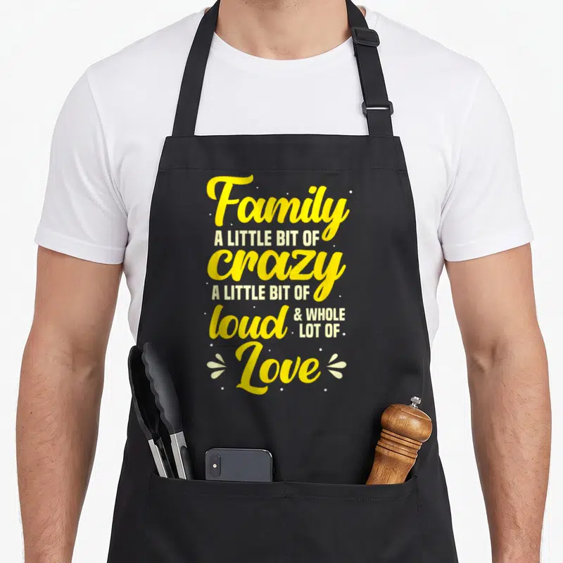 Bit gathering apron - Yellow and white stacked text reading Family A Little Bit Of Crazy surrounded by dots — shown on a black cotton canvas apron against a white background