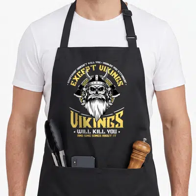 Sing songs about aprons - Viking skull with crossed axes and sarcastic text about killing in yellow and white — shown on a black cotton canvas apron against a white background