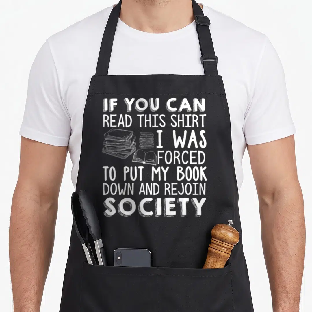 Read funny book apron - White stacked text quote about books with illustrations of book stacks and an open book — shown on a black cotton canvas apron against a white background