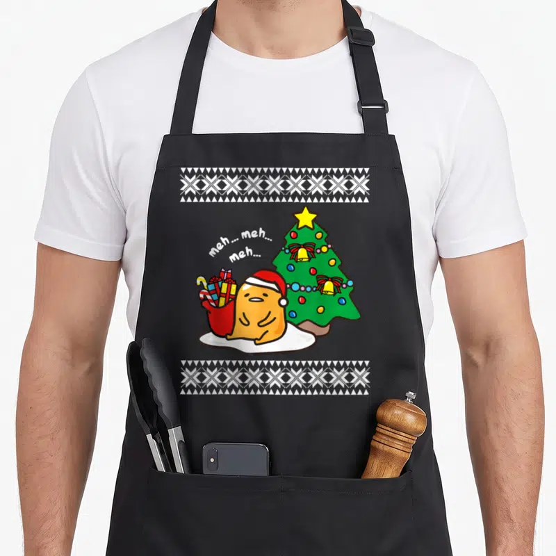 Gudetama ugly christmas sweater apron - Orange bird in Santa hat next to green tree with meh text and two white — shown on a black cotton canvas apron against a white background