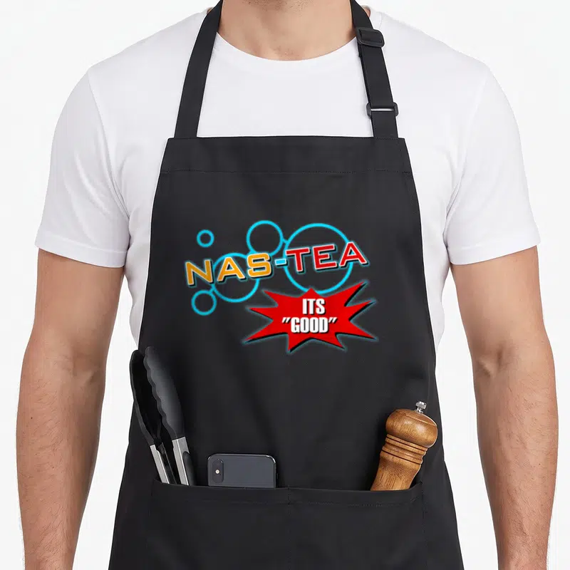 Nas tea apron - NAS-TEA ITS GOOD text in orange red light blue and white comic burst design — shown on a black cotton canvas apron against a white background