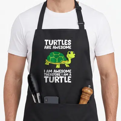 Therefore turtle apron - Green cartoon turtle with white text reading TURTLES ARE AWESOME I AM AWESOME THEREFORE I AM — shown on a black cotton canvas apron against a white background