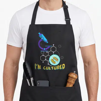 Biology microbiologist apron - Cartoon microscope, hexagonal chemical structure, petri dish with bacteria, and yellow — shown on a black cotton canvas apron against a white background