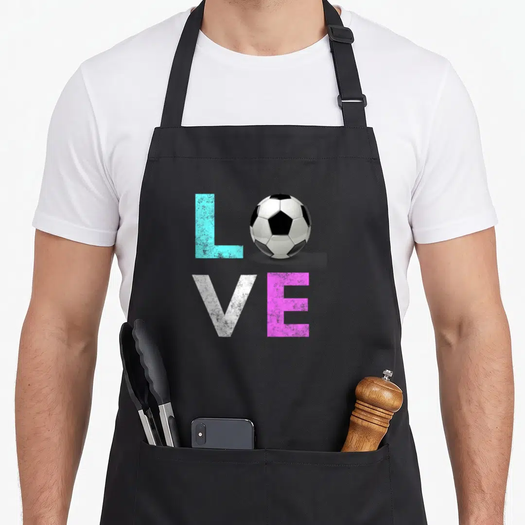 Funny soccer birthday apron - LOVE text with soccer ball replacing O in blue pink white and black — shown on a black cotton canvas apron against a white background