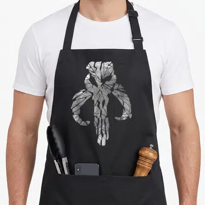 Clan skull apron - White cracked skull with horns on black background, distressed texture — shown on a black cotton canvas apron against a white background