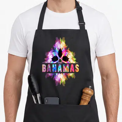 Cultural bahamian apron - Abstract tie-dye shape in purple pink yellow blue with BAHAMAS text overlay — shown on a black cotton canvas apron against a white background