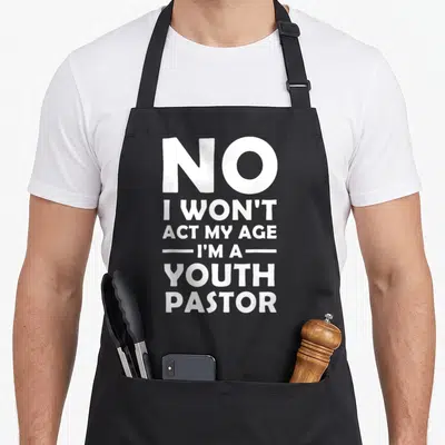Pastor preacher christian apron - White stacked text reading No I Won't Act My Age I'm A Youth Pastor — shown on a black cotton canvas apron against a white background
