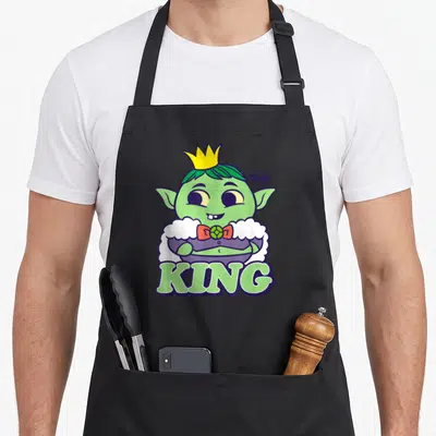 Troll king apron - Cartoon green character with yellow crown and KING text on white cloud background — shown on a black cotton canvas apron against a white background