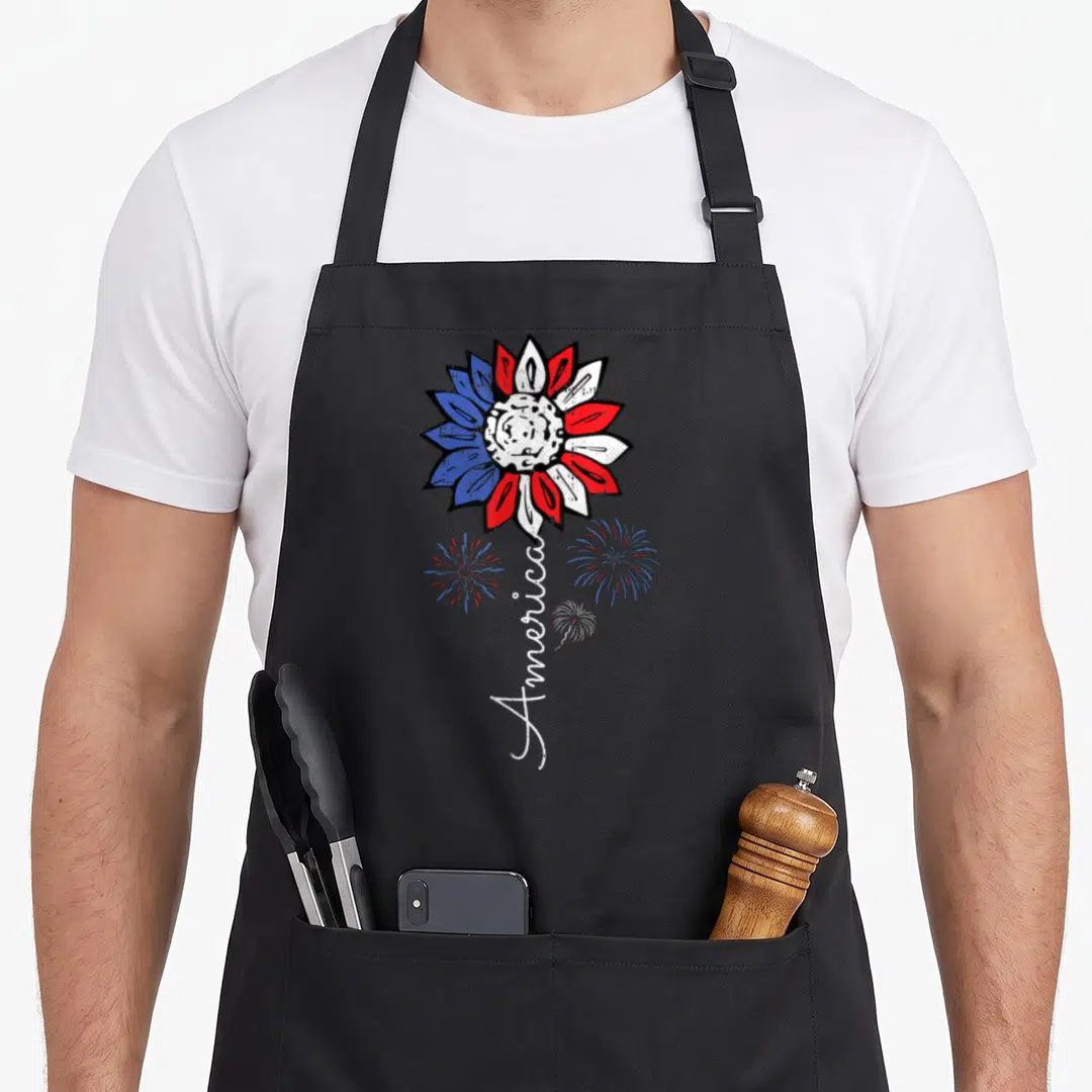 Sunflower 4th of july apron - Red white and blue sunflower with vertical America text and three fireworks — shown on a black cotton canvas apron against a white background