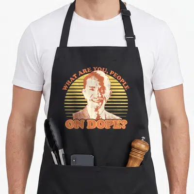 Fast mr apron - Distressed man portrait with orange text WHAT ARE YOU PEOPLE ON DOPE over yellow striped sun — shown on a black cotton canvas apron against a white background
