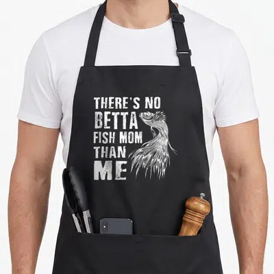 Vintage betta fish apron - White text THERE'S NO BETTA FISH MOM THAN ME with line-art betta fish — shown on a black cotton canvas apron against a white background
