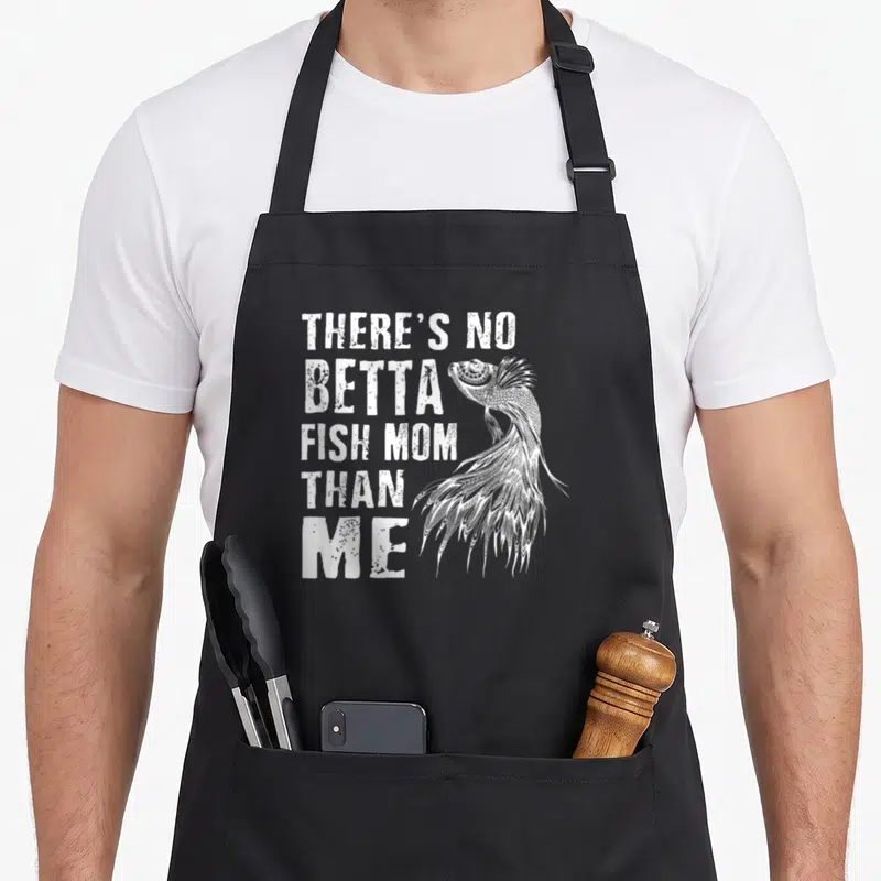 Vintage betta fish apron - White text THERE'S NO BETTA FISH MOM THAN ME with line-art betta fish — shown on a black cotton canvas apron against a white background