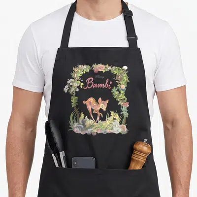 Portrait floral apron - Bambi fawn in watercolor wreath with rabbits birds pink flowers green leaves brown accents — shown on a black cotton canvas apron against a white background