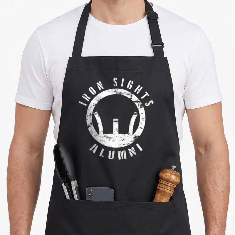 Sight shooting apron - Distressed white circle with Iron Sights Alumni text and abstract M-16 sight shape — shown on a black cotton canvas apron against a white background