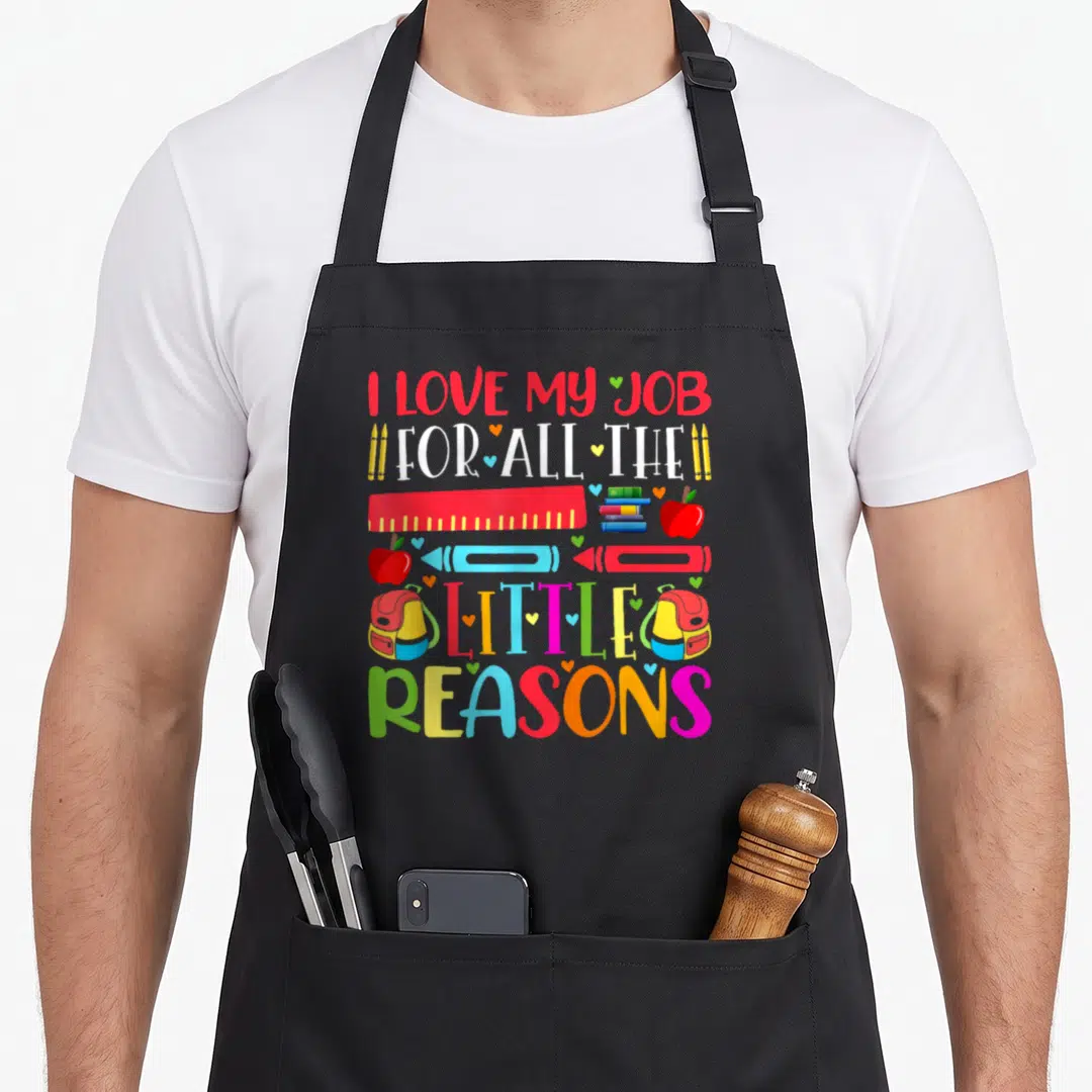 Vintage reason teacher apron - Stacked text I love my job with ruler, books, apples, backpacks and hearts in red blue — shown on a black cotton canvas apron against a white background