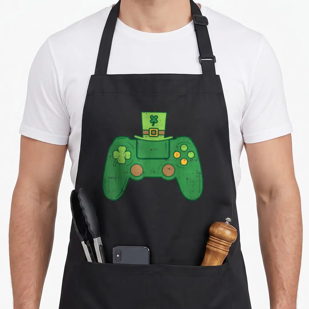 Video irish aprons - Green game controller with top hat shamrock yellow buckle cartoon design — shown on a black cotton canvas apron against a white background