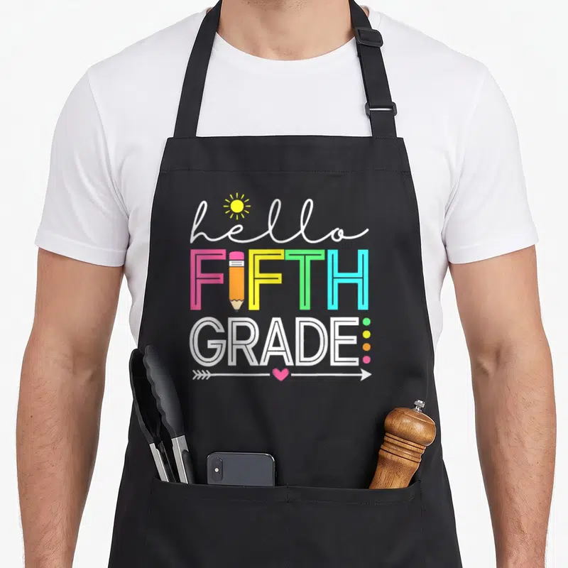Student 5th teacher apron - hello FIFTH GRADE text with sun pencil arrow and heart in white pink yellow green blue — shown on a black cotton canvas apron against a white background