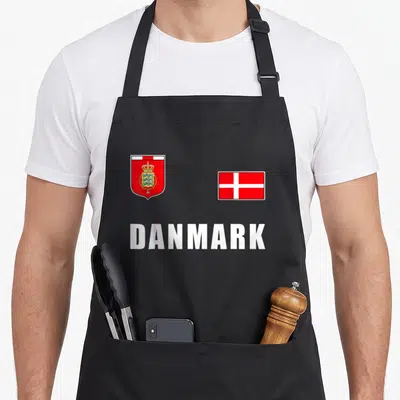 Danmark denmark apron - Coat of arms and flag above white DANMARK text in red and gold — shown on a black cotton canvas apron against a white background