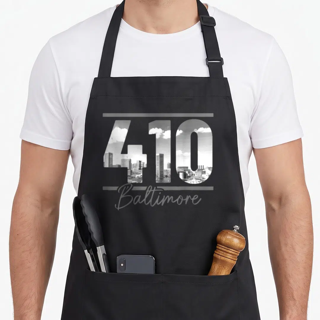 Baltimore city skyline apron - 410 number filled with grayscale Baltimore skyline and script Baltimore text between two — shown on a black cotton canvas apron against a white background