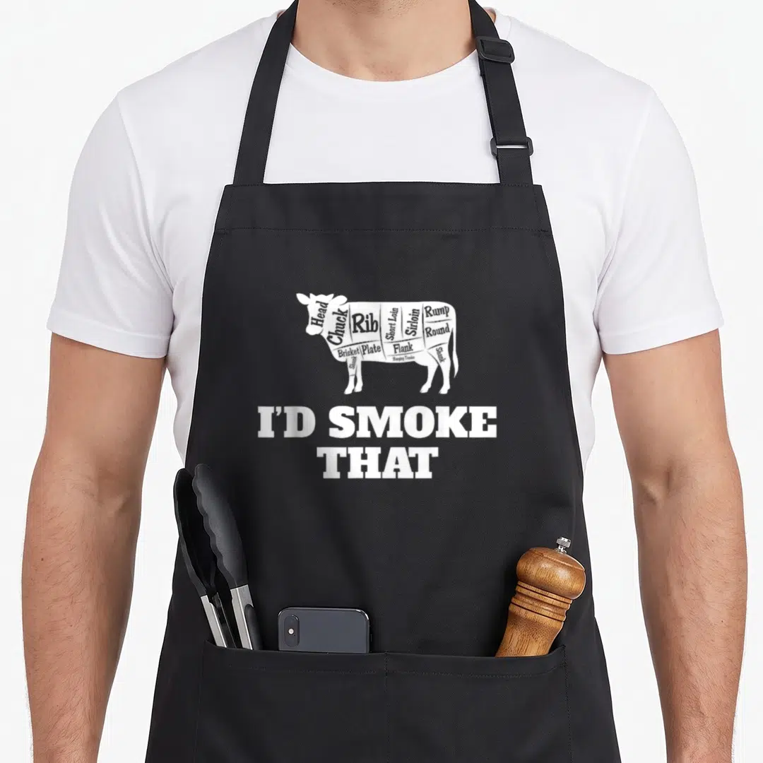 King smoke master apron - White cow silhouette divided into meat cuts with labels and I'D SMOKE THAT text below — shown on a black cotton canvas apron against a white background