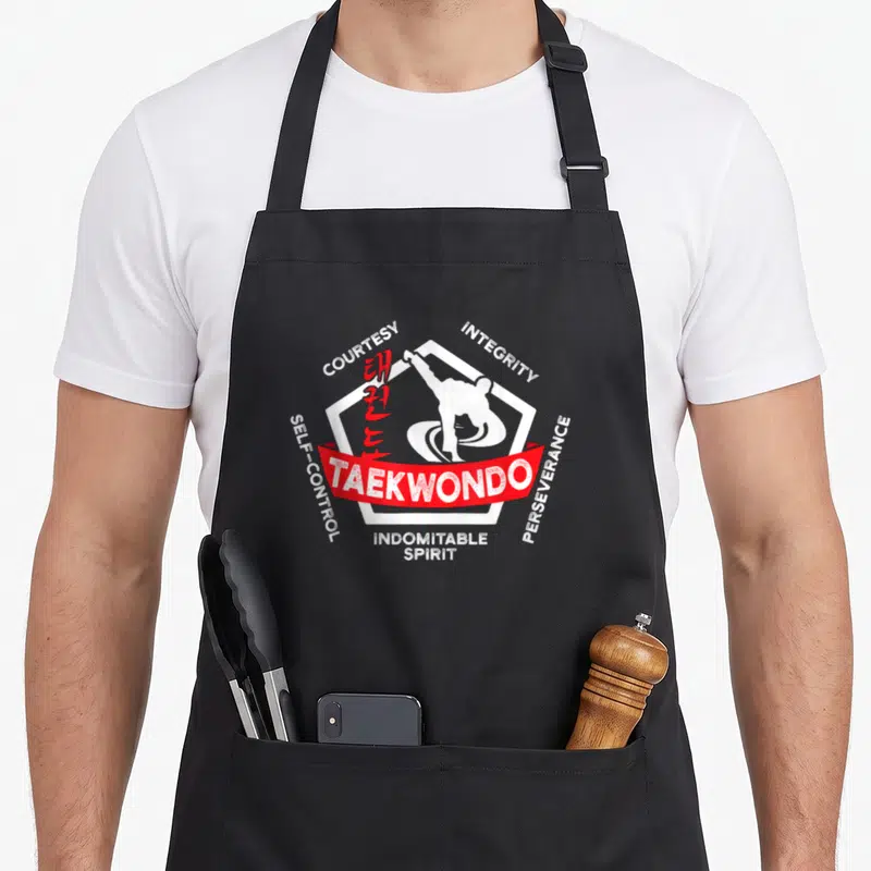Martial taekwondo apron - Whit hexagon with kicker, red ribbon, and five tenet words — shown on a black cotton canvas apron against a white background