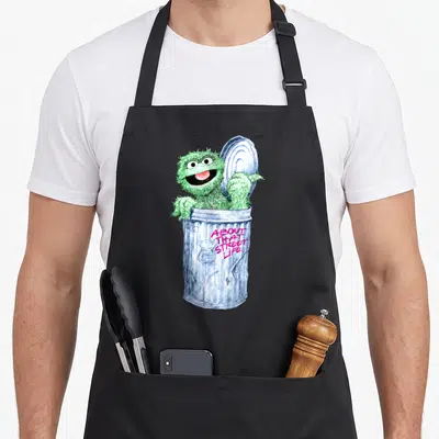 Funny oscar the grouch apron - Green monster in blue trash can with pink About That Street Life text — shown on a black cotton canvas apron against a white background